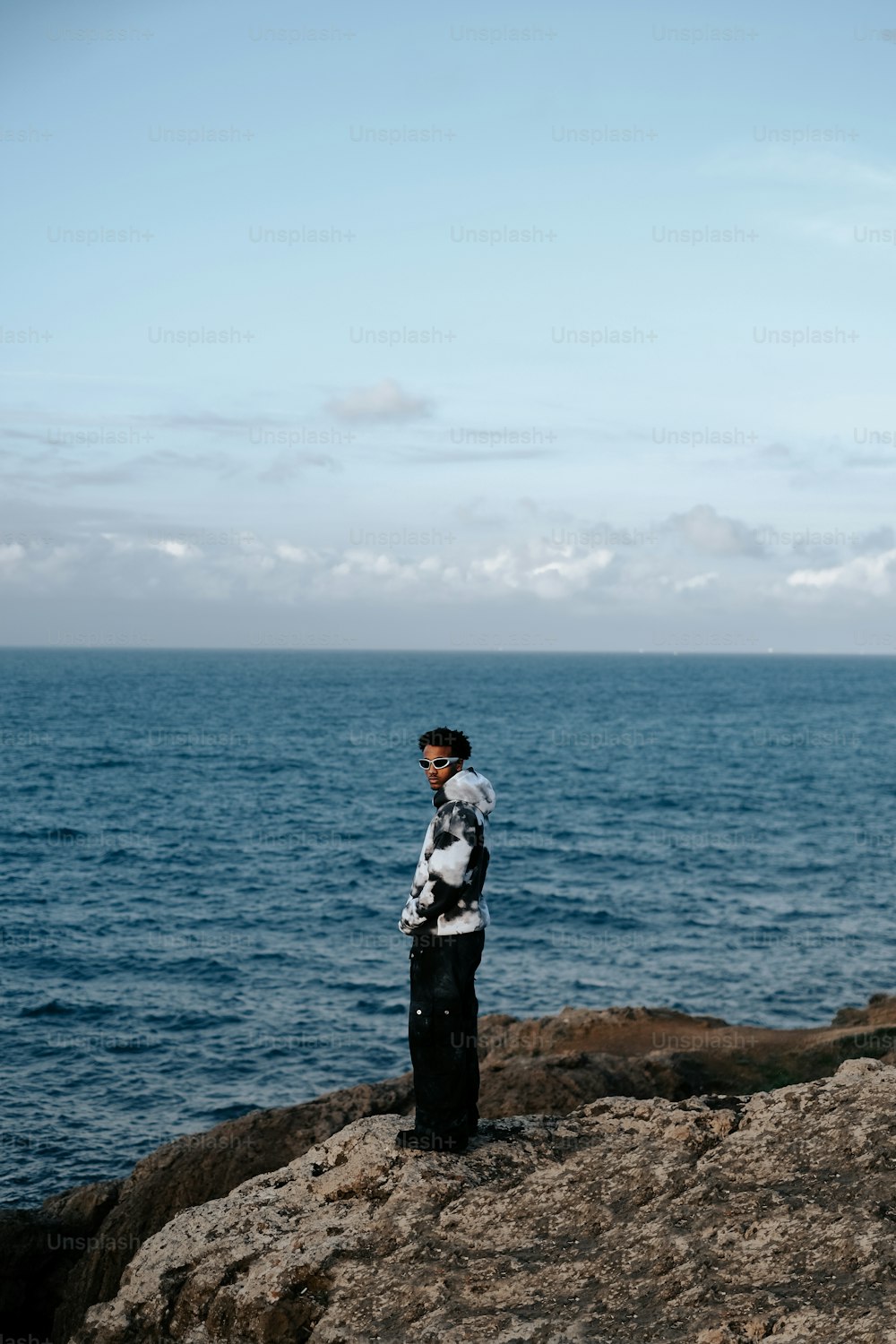 um homem de pé em cima de uma rocha ao lado do oceano