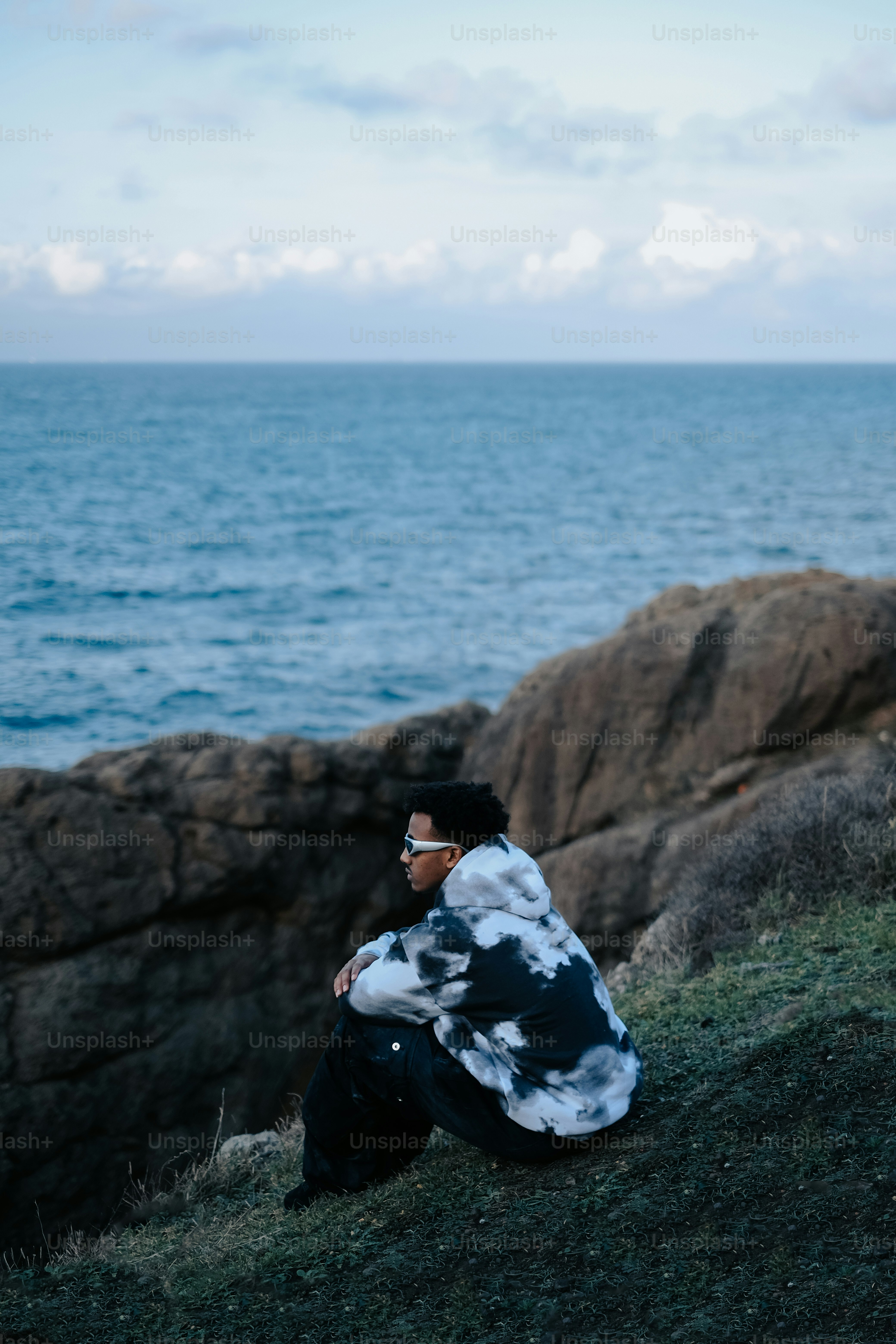 海の隣の丘に座っている男