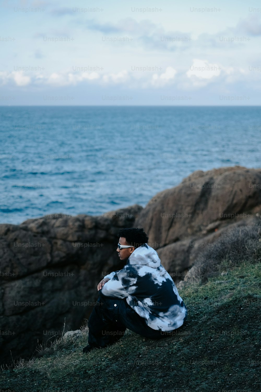 um homem sentado em uma colina ao lado do oceano