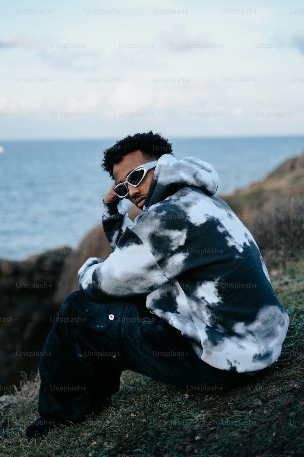 a man sitting on top of a hill next to the ocean