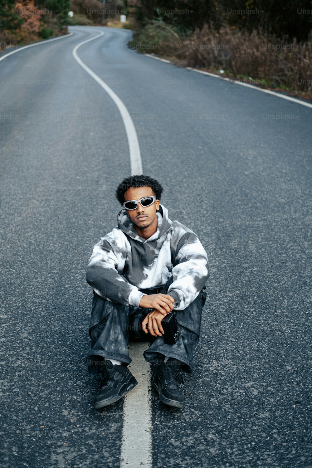 a man sitting on the side of a road wearing sunglasses