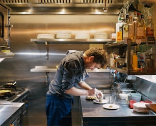 Un hombre en una cocina preparando comida en un plato