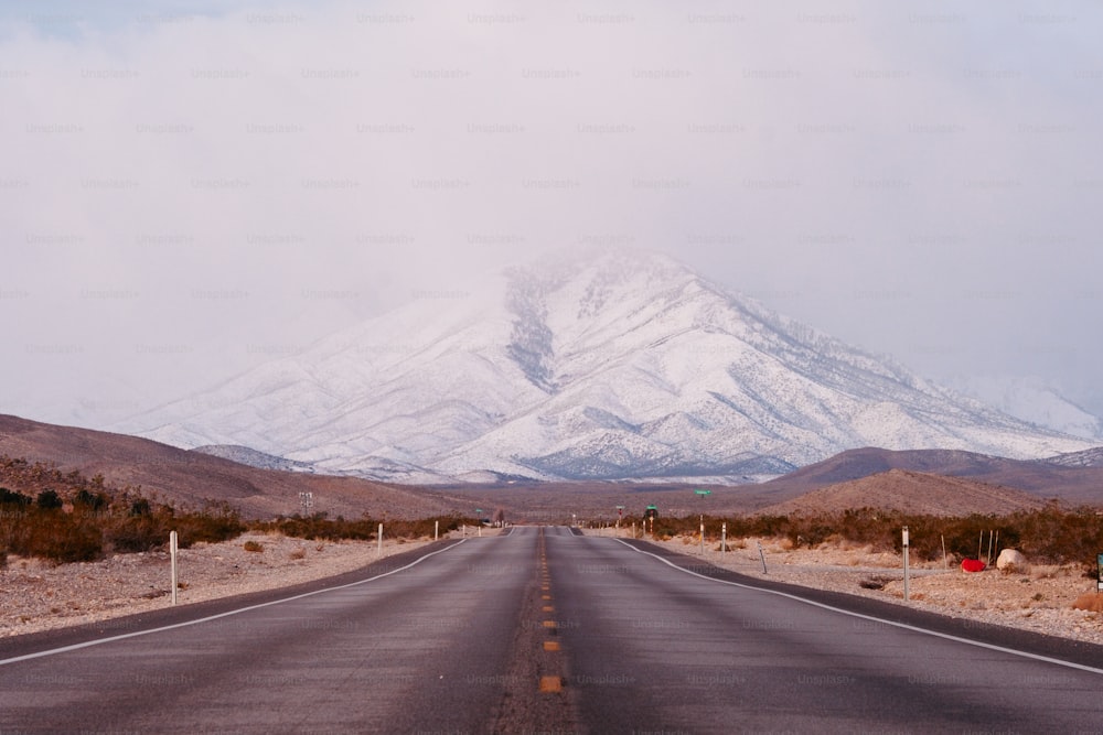 an empty road with a snow covered mountain in the background