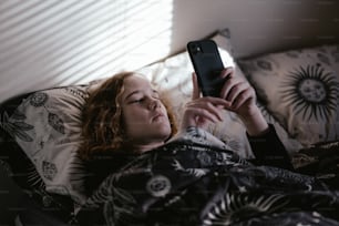 Una donna sdraiata sul letto che guarda il suo telefono