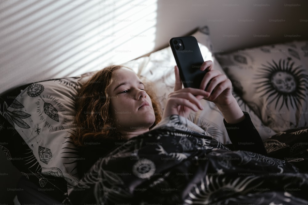 uma mulher deitada na cama olhando para o telefone dela