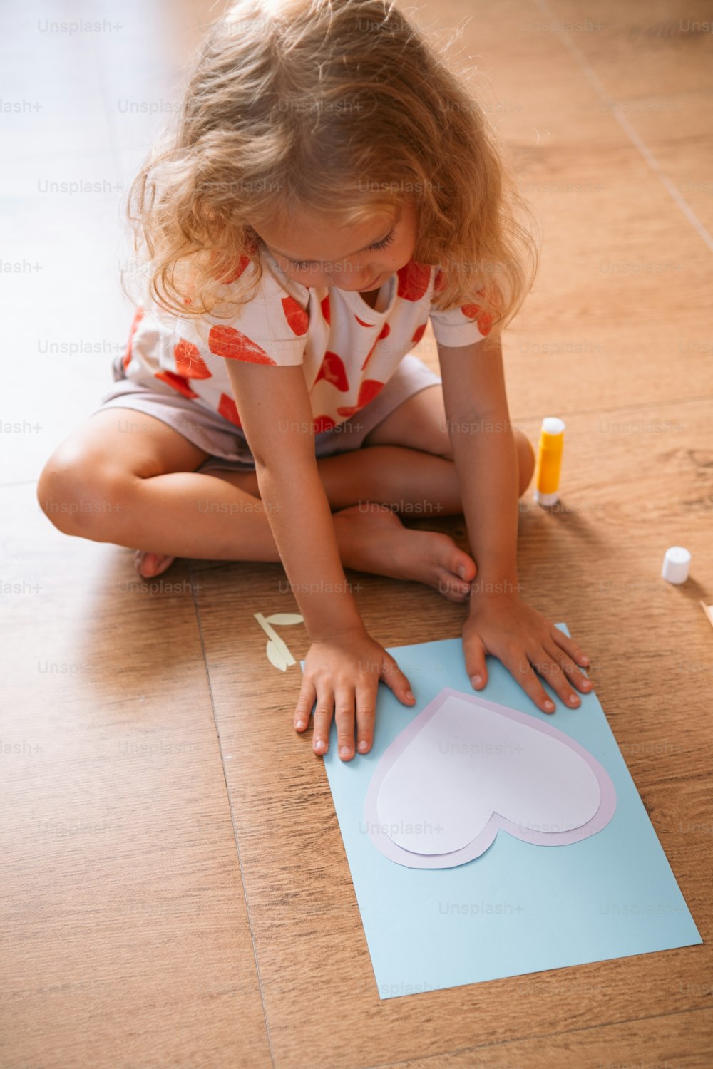 a little girl sitting on the floor making a paper cloud