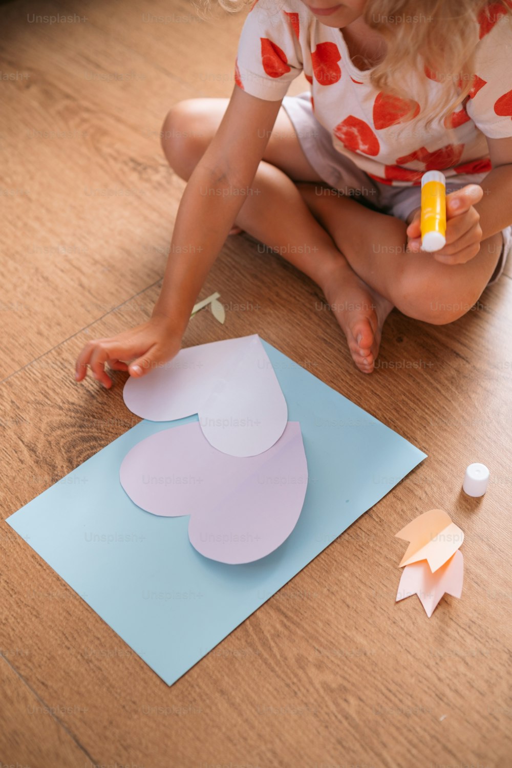a little girl sitting on the floor making a paper heart