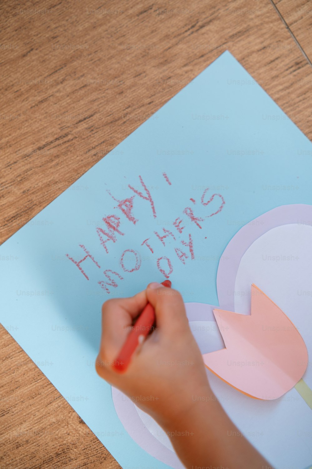 a child's hand writing happy mothers day on a piece of paper