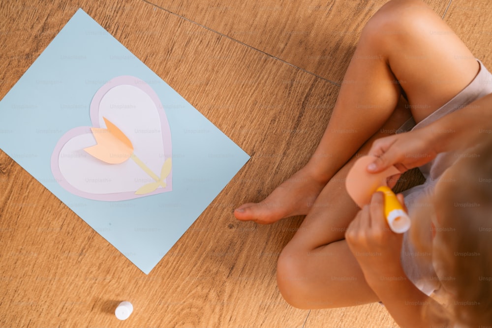 a little girl sitting on the floor cutting out a paper heart