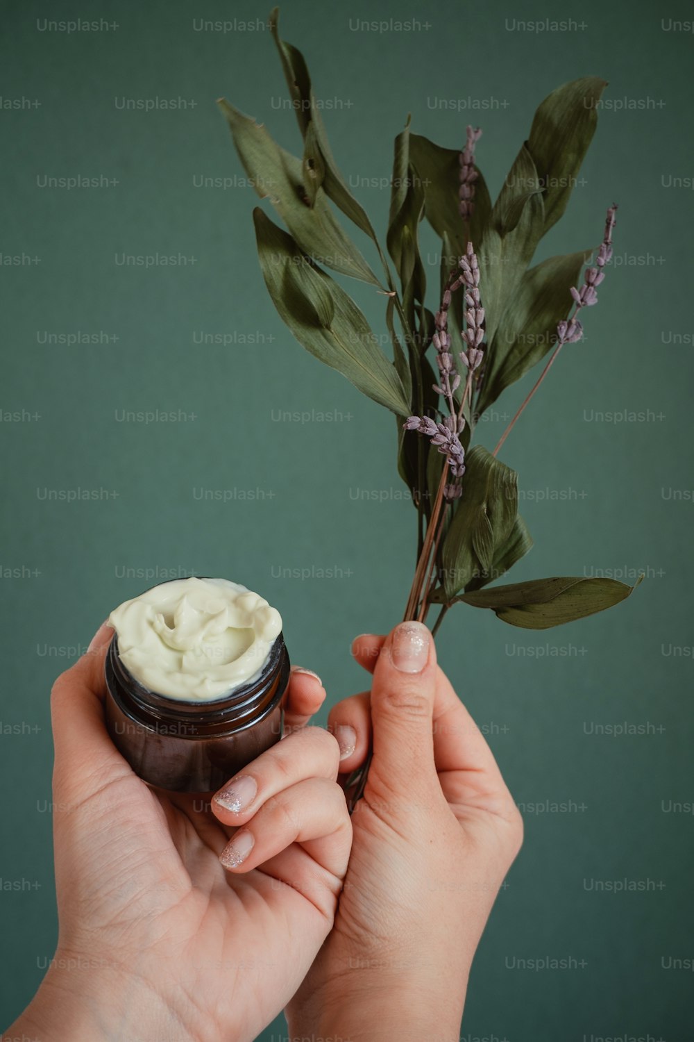 a hand holding a jar of cream next to a plant