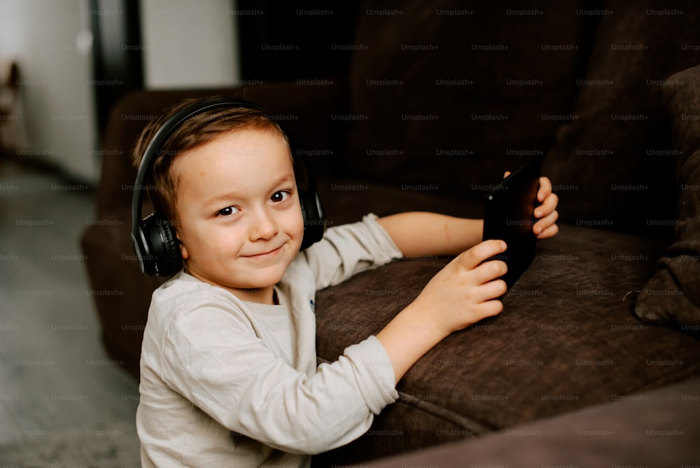 Ein kleiner Junge mit Kopfhörern auf einer Couch