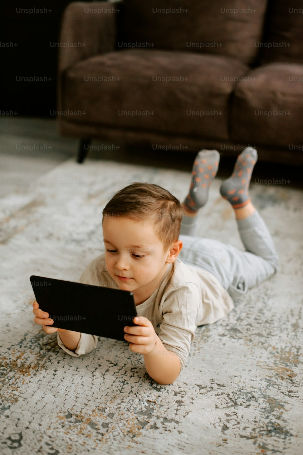 a little boy laying on the floor playing with a tablet
