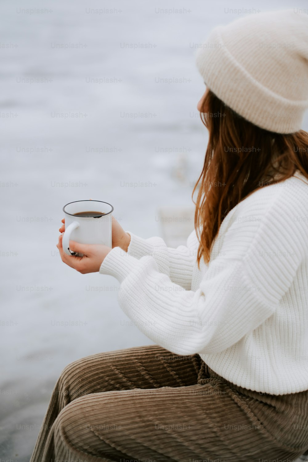 una donna seduta su un molo che tiene in mano una tazza di caffè