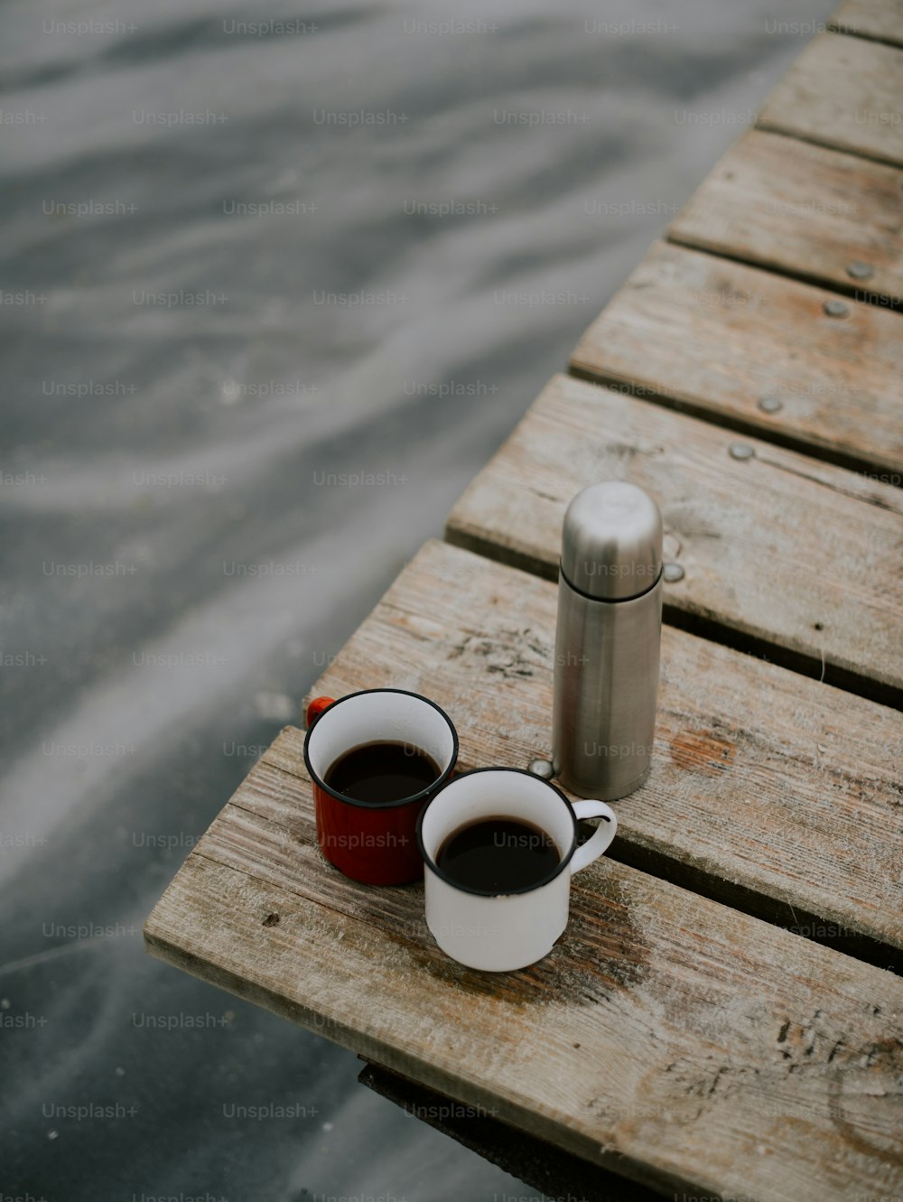 Dos tazas de café sentadas en un muelle de madera