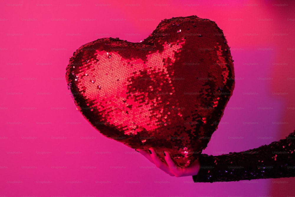 a woman holding a heart shaped sequin pillow