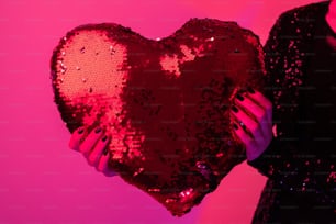a woman holding a heart shaped sequin pillow