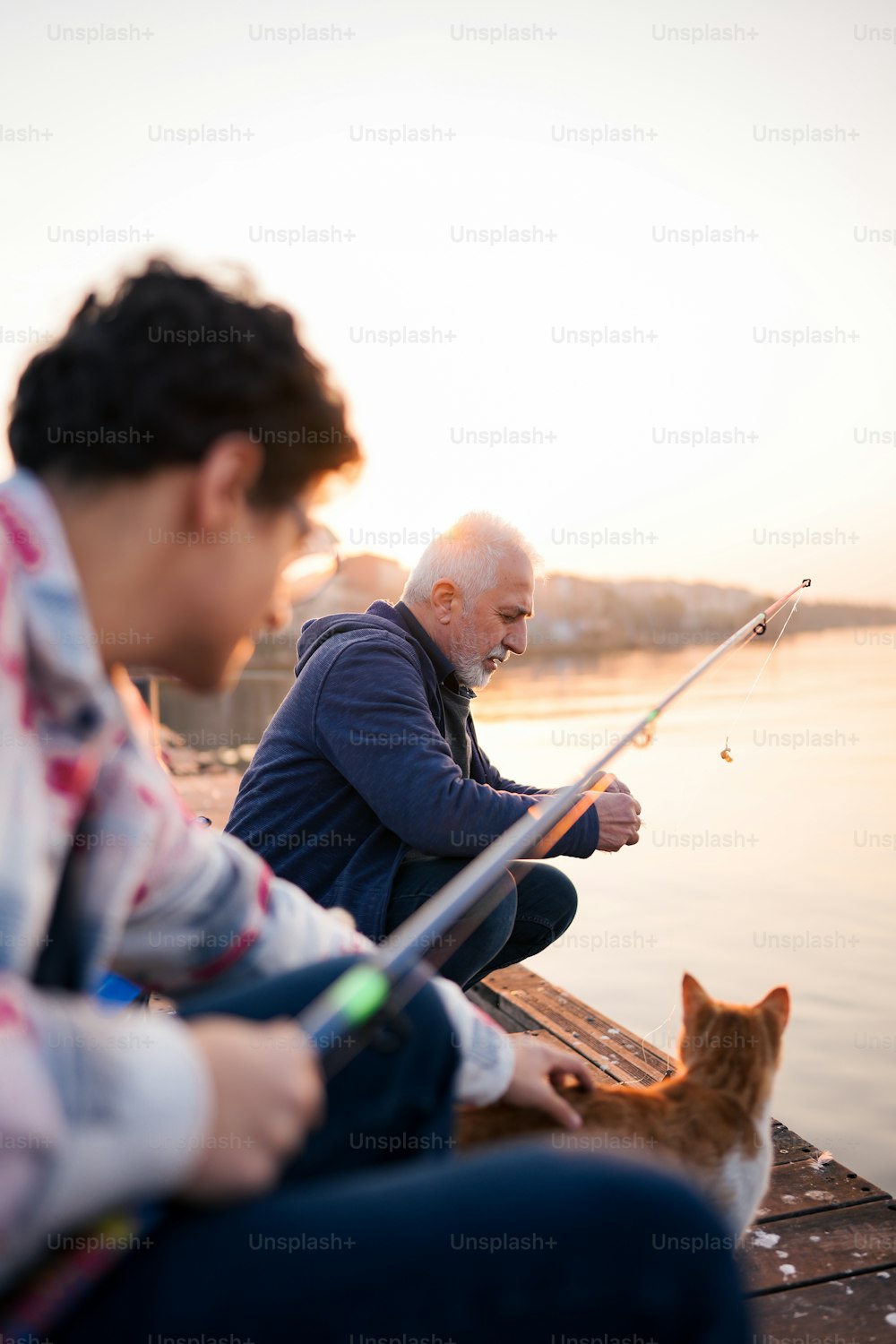 a man and a woman sitting on a dock with a cat