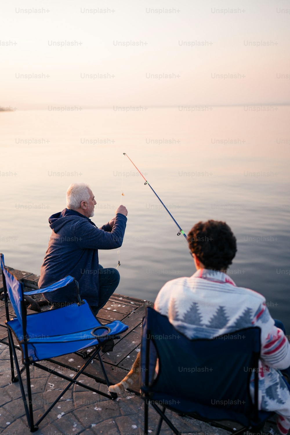 A man sitting in a chair fishing from a pier photo – Fishing Image
