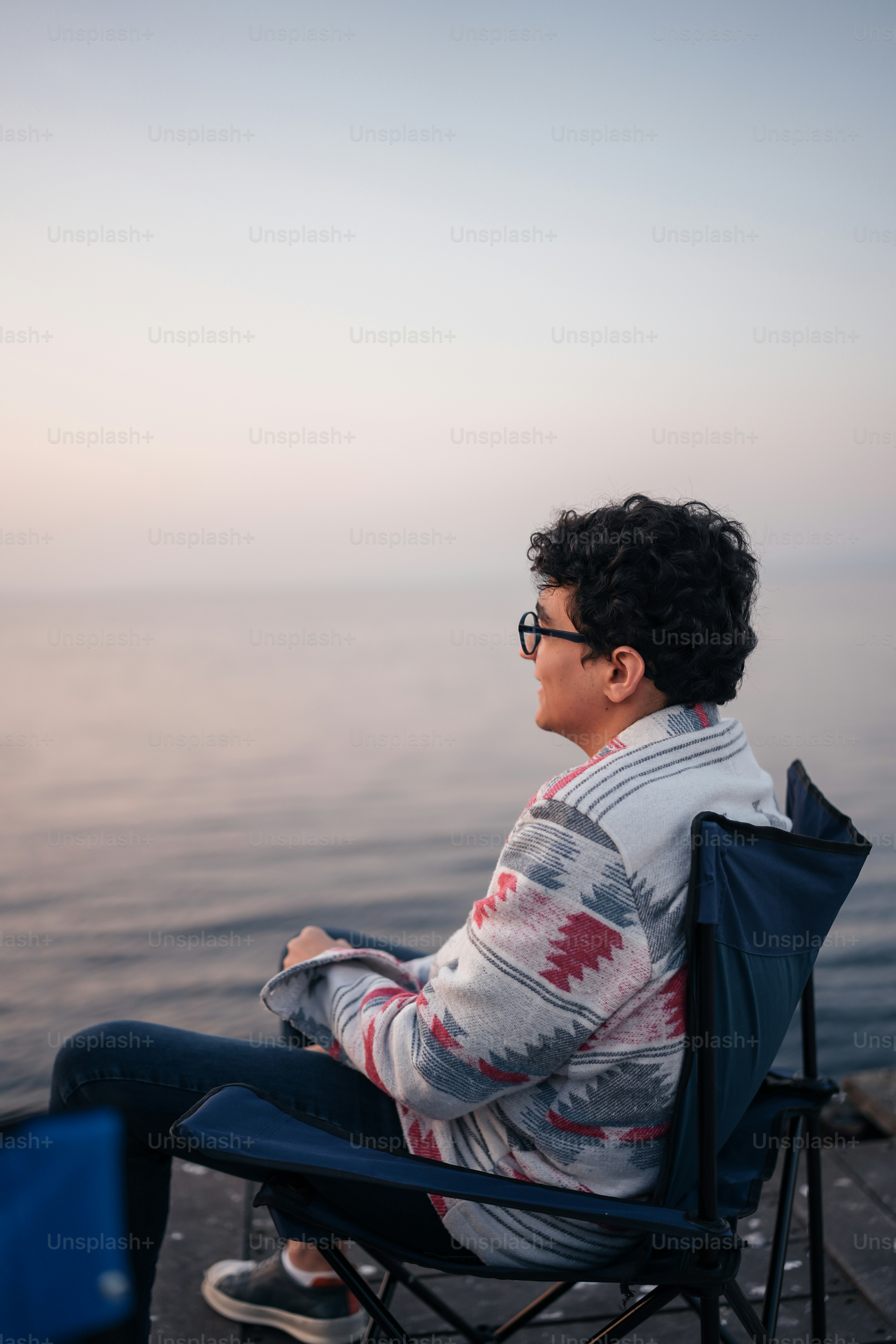 A man sitting in a chair looking out at the water photo – Sitting Image ...