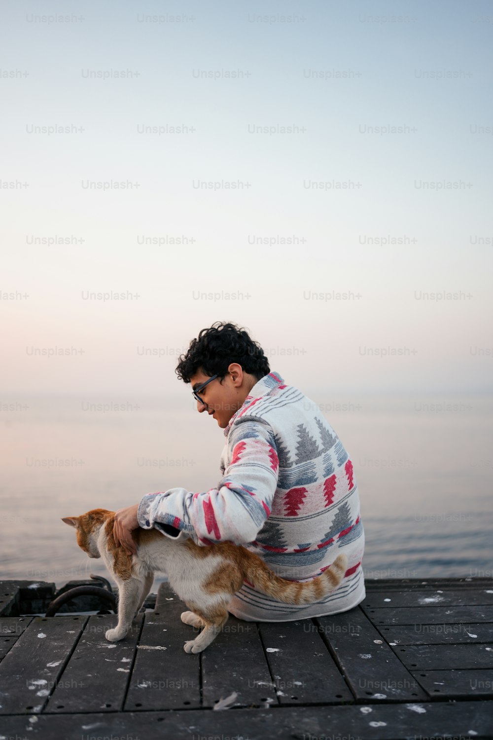 a man sitting on a dock petting a cat