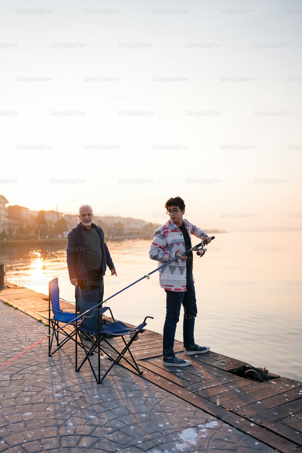 a couple of men standing on top of a pier next to a body of water