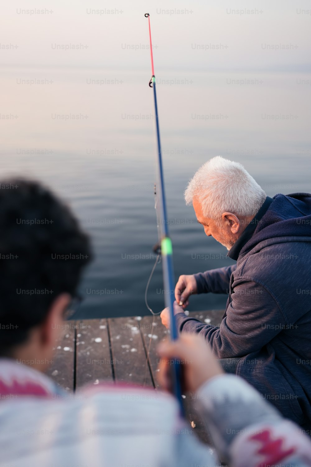 A man sitting on a dock while holding a fishing pole photo – Hook