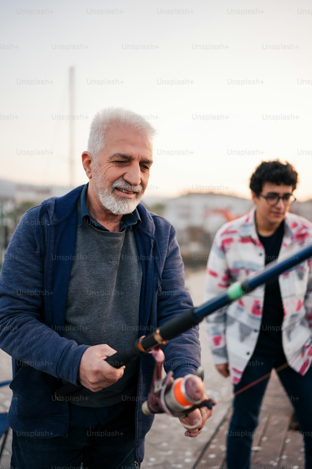 an older man holding a fishing rod while another man looks on