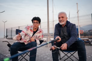 a man sitting in a chair next to another man holding a fishing pole