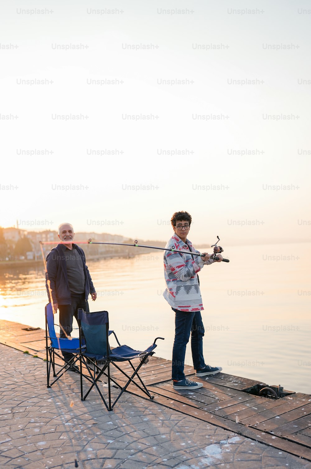 two people standing on a dock with a fishing rod