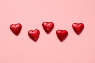 Quattro caramelle rosse a forma di cuore su uno sfondo rosa