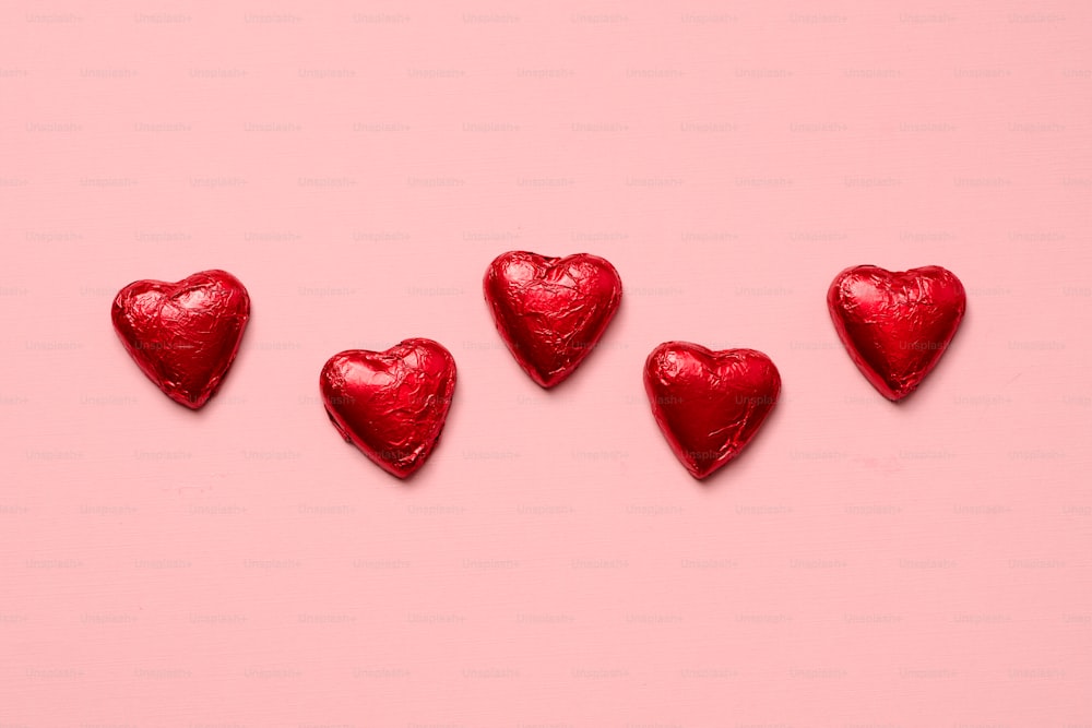four red heart shaped candies on a pink background