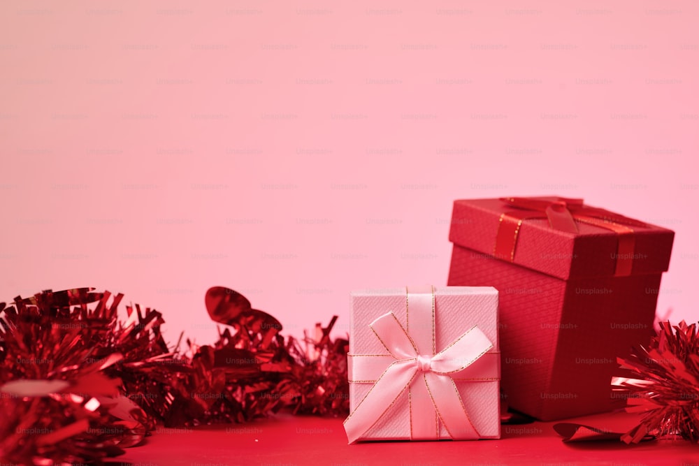 a red gift box with a white bow sitting next to a red tinsel tin