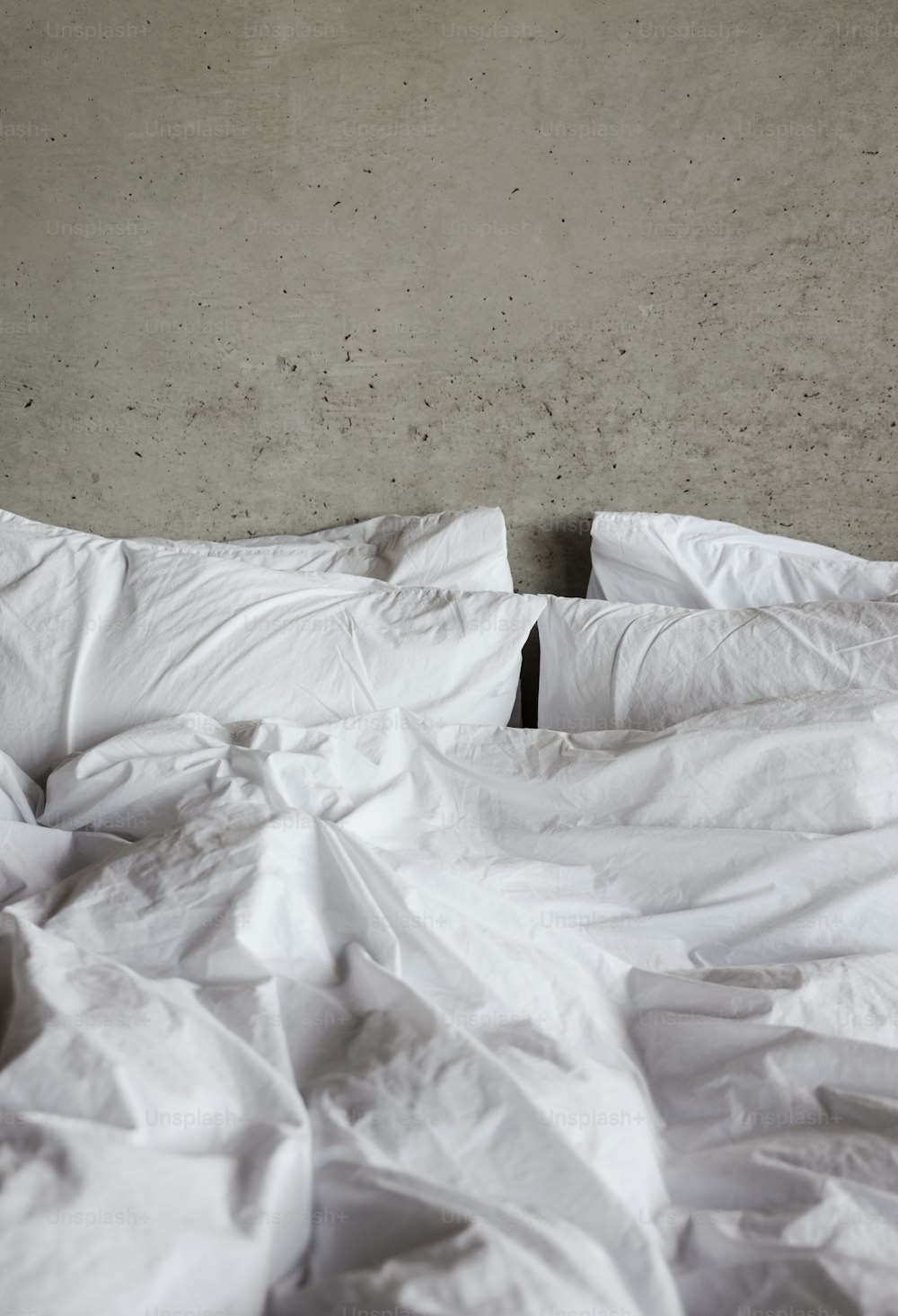 an unmade bed with white sheets and pillows