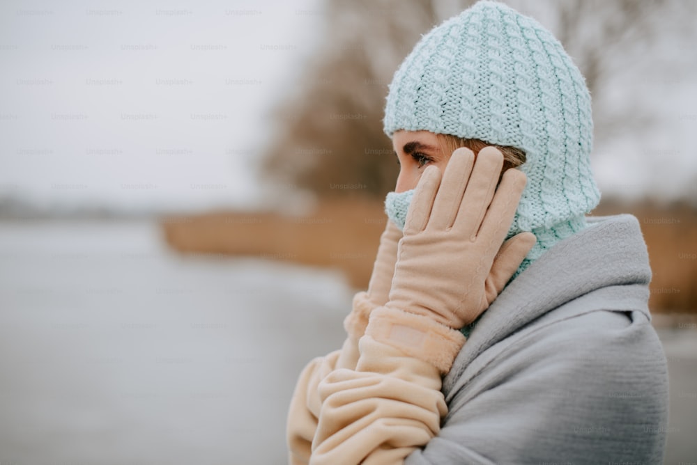 a woman wearing a winter hat and mittens covers her face