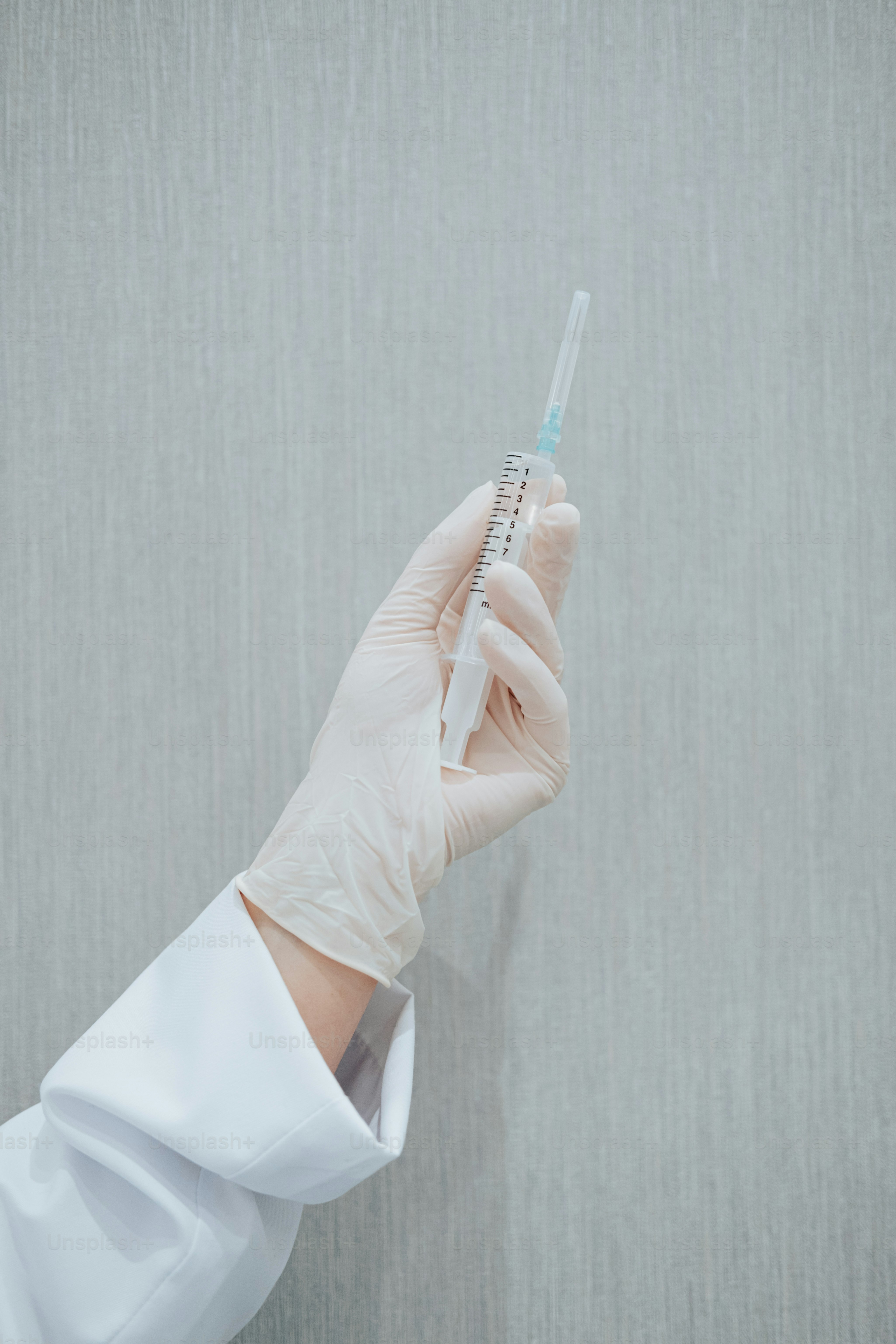 a person in a white coat and gloves holding a sy