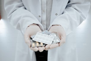 une personne en blouse de laboratoire tenant un paquet de pilules