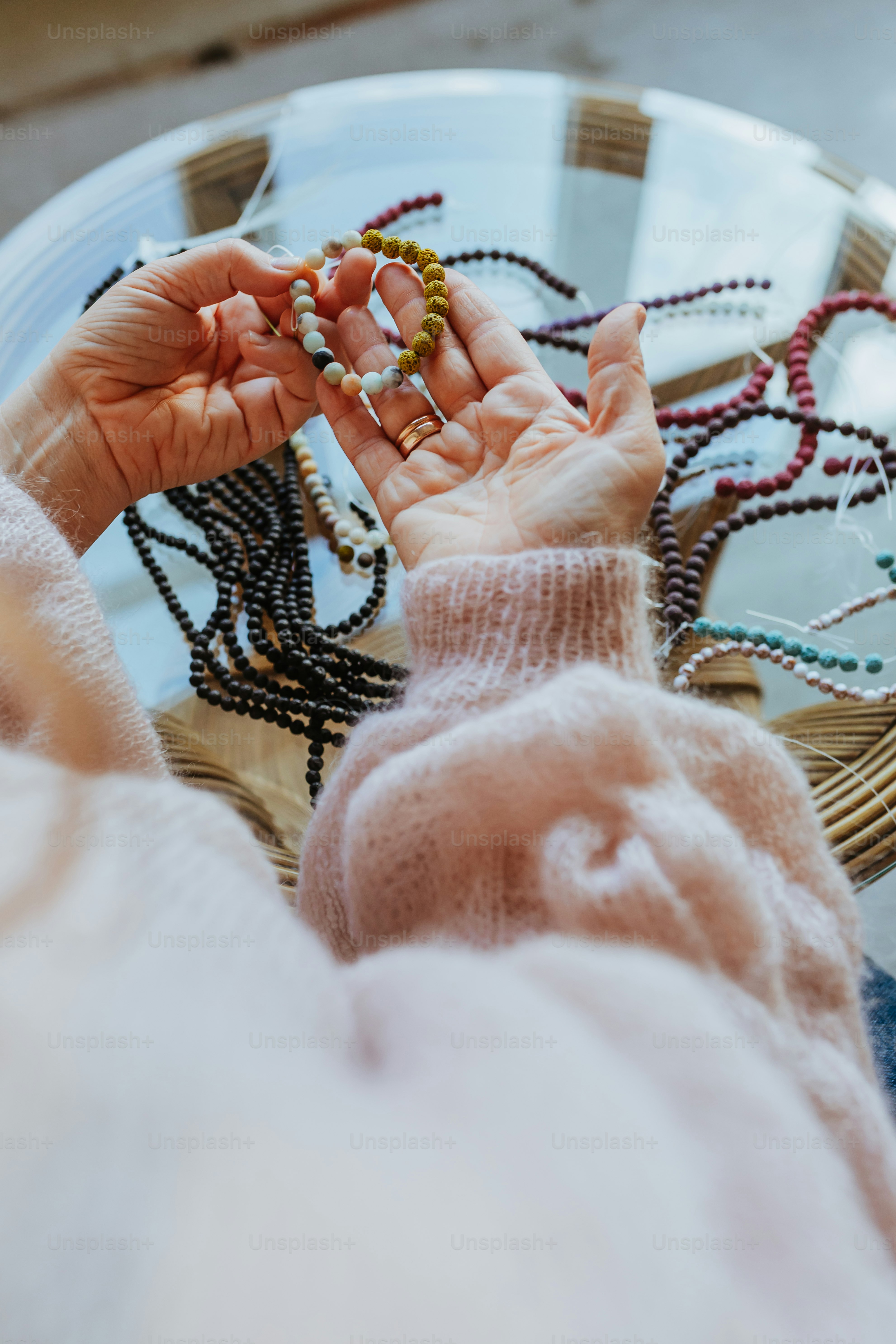 a person holding a beaded bracelet on top of a glass table