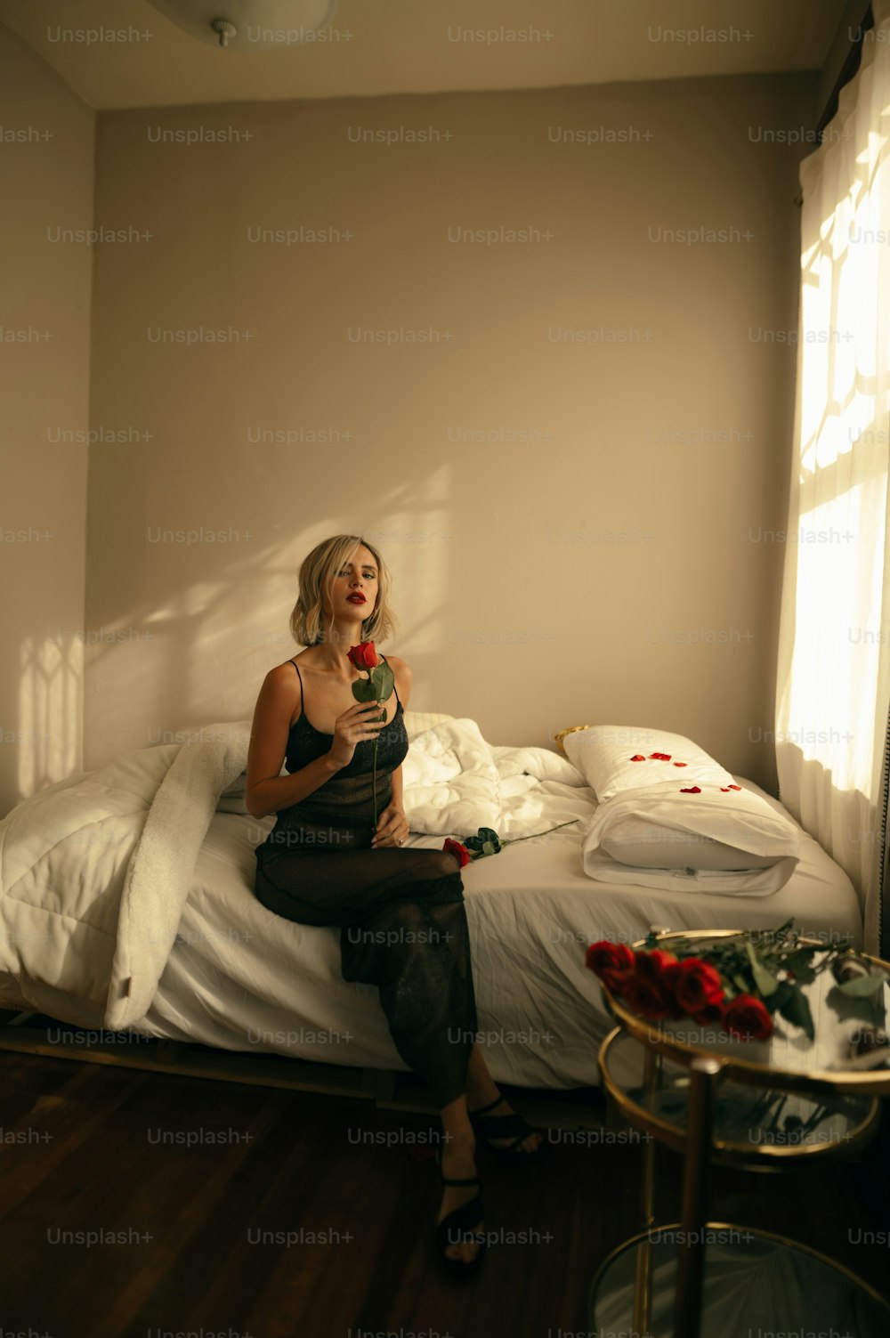 uma mulher sentada em cima de uma cama ao lado de uma janela