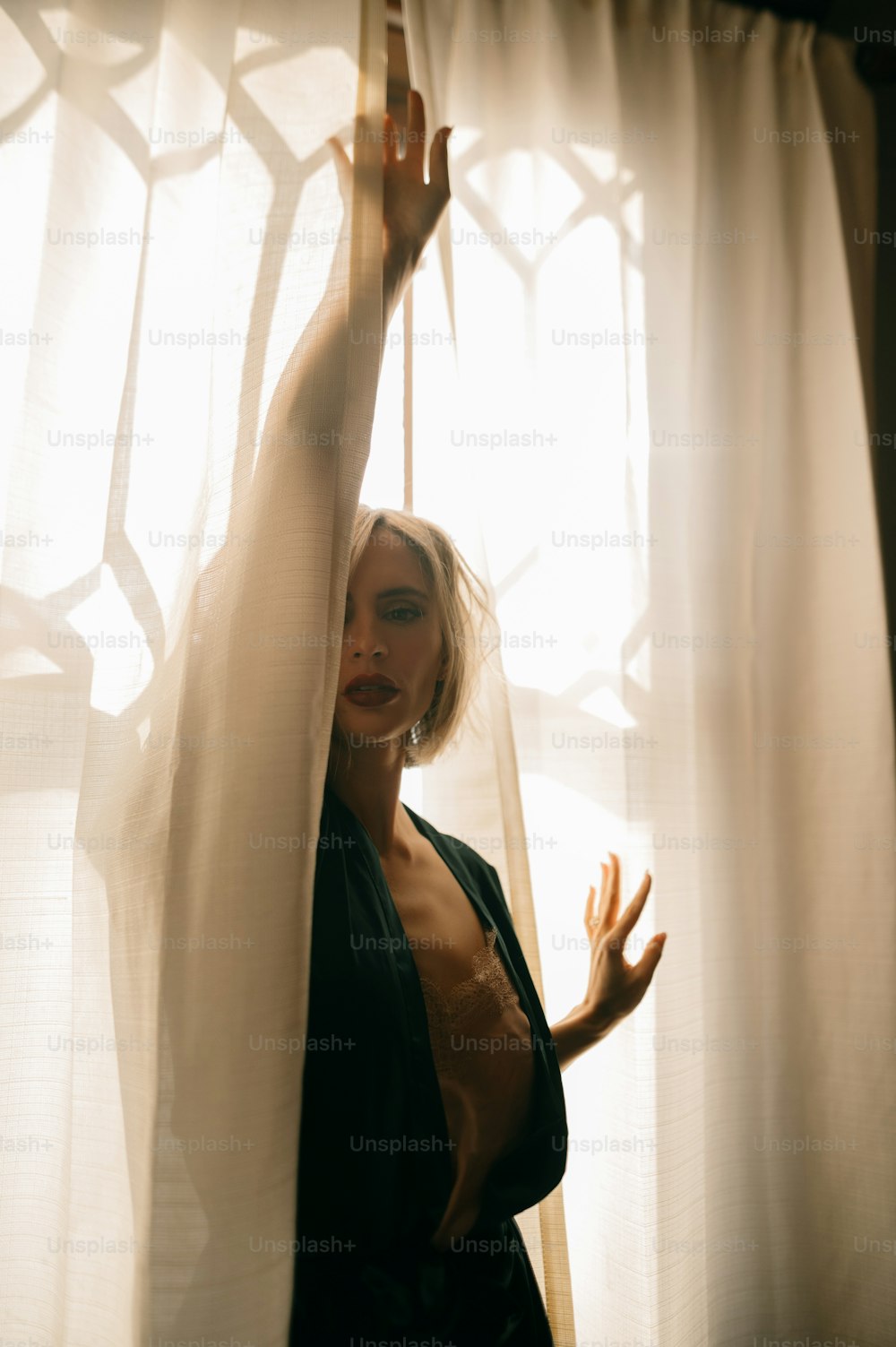 a woman standing in front of a window with sheer curtains