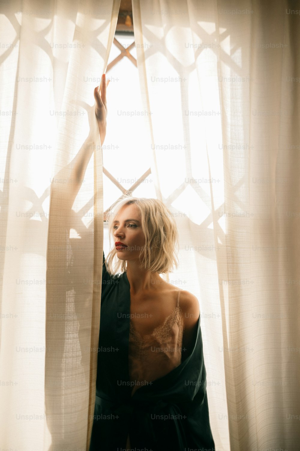 uma mulher em pé na frente de uma janela ao lado de uma cortina