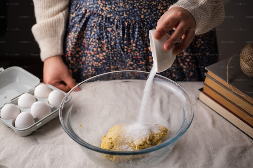 a person pouring flour into a glass bowl