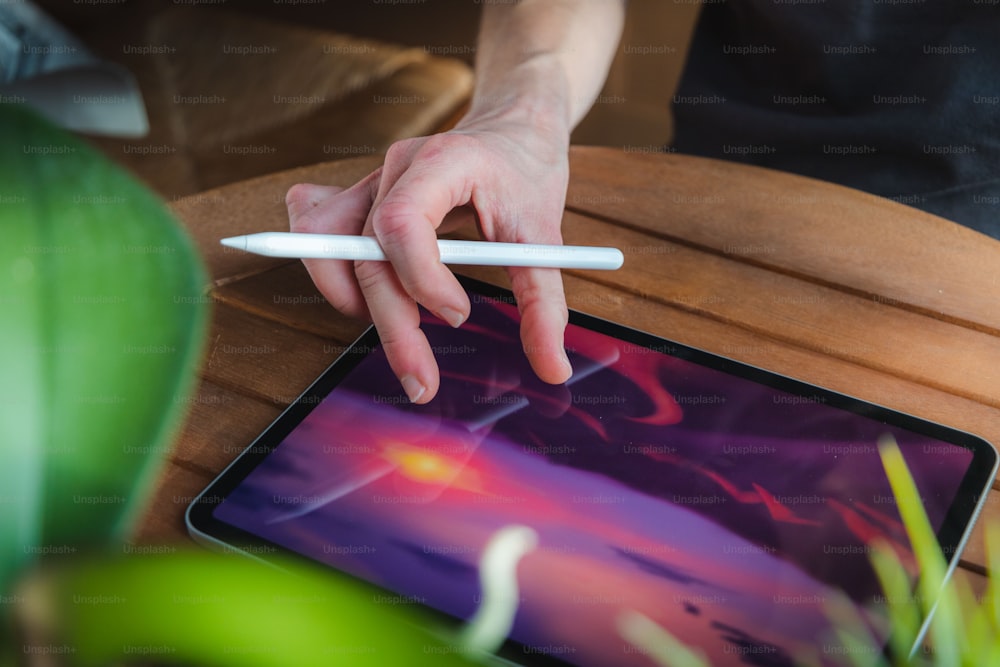 a person's hand holding a pen over a tablet