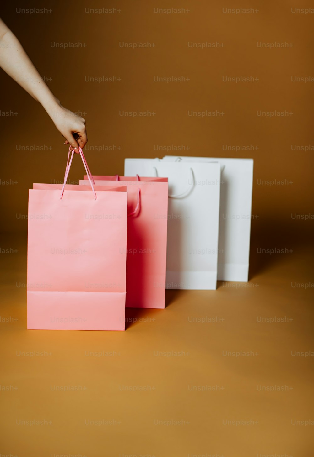 Una persona sosteniendo una bolsa de compras rosa frente a tres bolsas de compras blancas
