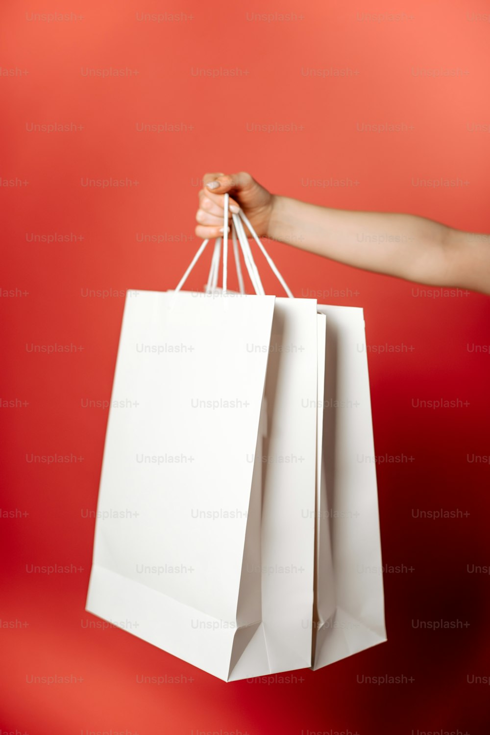 a hand holding a white shopping bag against a red background
