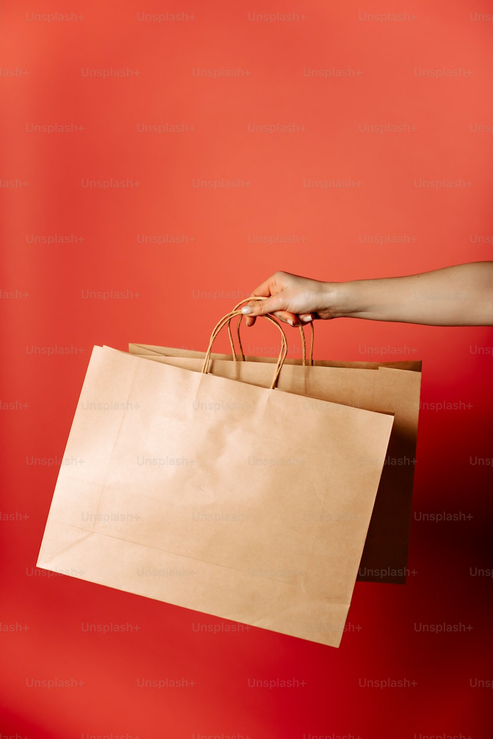 una mano che tiene un sacchetto di carta marrone su uno sfondo rosso