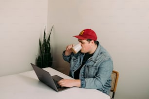 a man sitting at a table with a laptop drinking from a cup