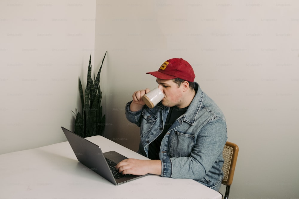 um homem sentado em uma mesa com um laptop bebendo de um copo