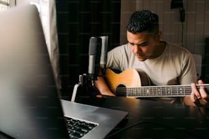 노트북 앞에 앉아 기타를 연주하는 남자