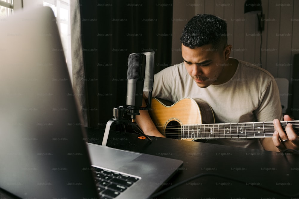 um homem sentado na frente de um laptop tocando uma guitarra