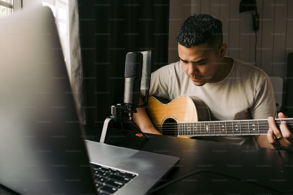 a man sitting in front of a laptop playing a guitar